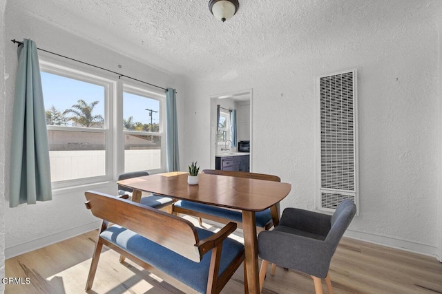 dining room with a textured ceiling, a heating unit, light wood-style floors, and a textured wall