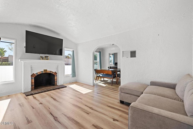 living area featuring lofted ceiling, light wood-style floors, arched walkways, and a textured wall