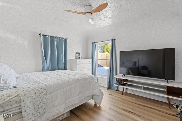 bedroom featuring ceiling fan, a textured ceiling, wood finished floors, and a textured wall