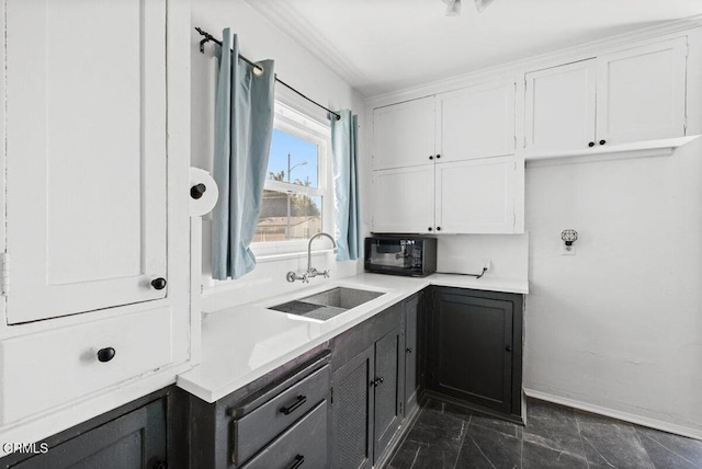 kitchen featuring light countertops, white cabinets, baseboards, and a sink