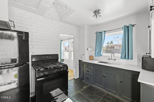 kitchen with black appliances, gray cabinetry, a sink, brick wall, and light countertops