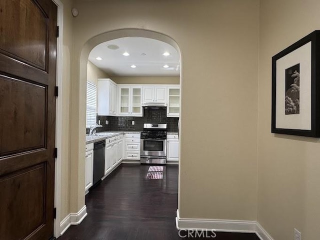 kitchen with stainless steel gas range oven, tasteful backsplash, black dishwasher, arched walkways, and white cabinets