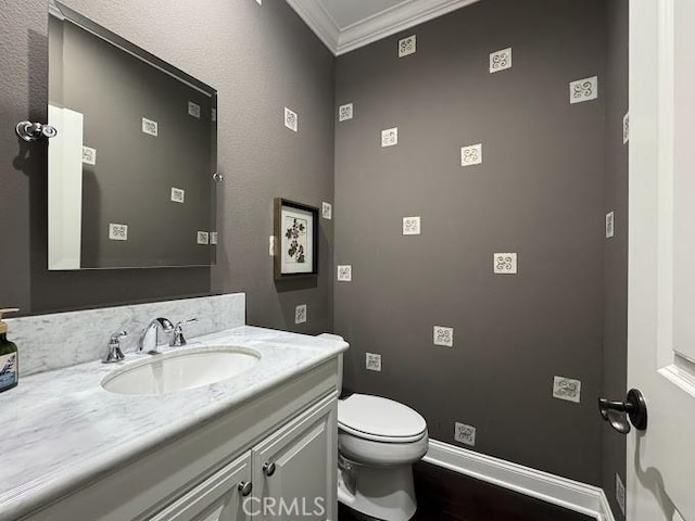 bathroom featuring toilet, ornamental molding, wood finished floors, baseboards, and vanity