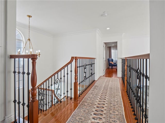 corridor featuring an upstairs landing, a notable chandelier, ornamental molding, and wood finished floors