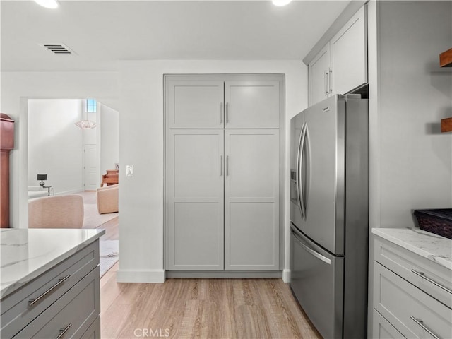 kitchen featuring light wood-type flooring, light stone countertops, stainless steel refrigerator with ice dispenser, and gray cabinetry