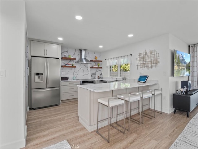 kitchen with open shelves, a peninsula, decorative backsplash, wall chimney range hood, and stainless steel fridge