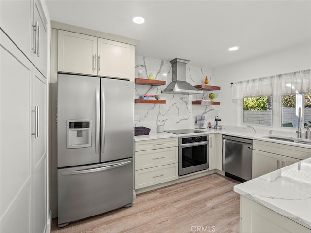 kitchen featuring light stone counters, open shelves, a sink, stainless steel appliances, and wall chimney exhaust hood