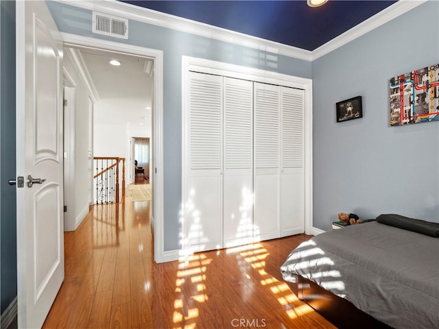 bedroom featuring visible vents, wood finished floors, a closet, crown molding, and baseboards