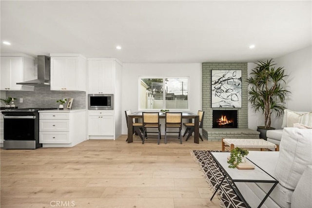 kitchen with light wood-style flooring, open floor plan, appliances with stainless steel finishes, wall chimney range hood, and decorative backsplash