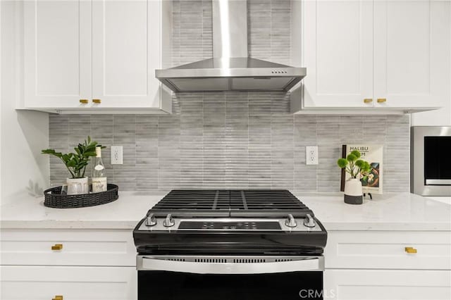 kitchen featuring light stone countertops, white cabinets, range with gas cooktop, wall chimney exhaust hood, and backsplash