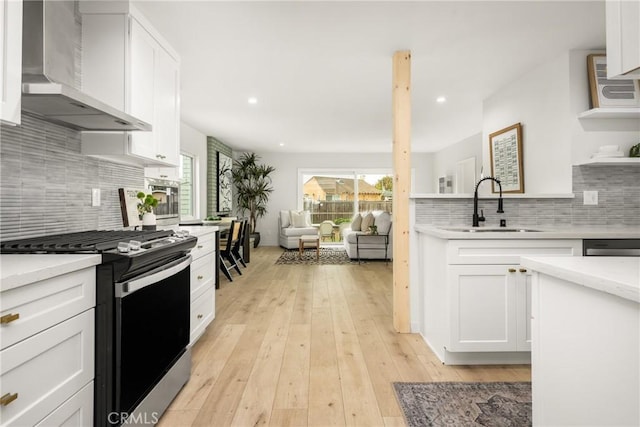 kitchen with gas stove, white cabinetry, wall chimney range hood, and a sink