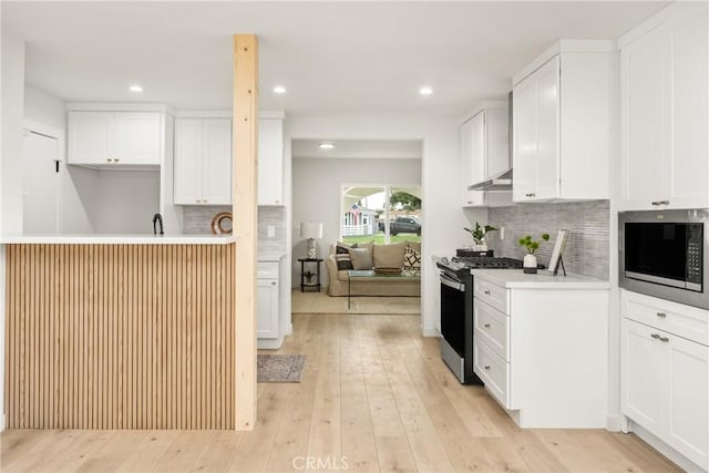 kitchen with under cabinet range hood, white cabinetry, light wood-style floors, appliances with stainless steel finishes, and light countertops