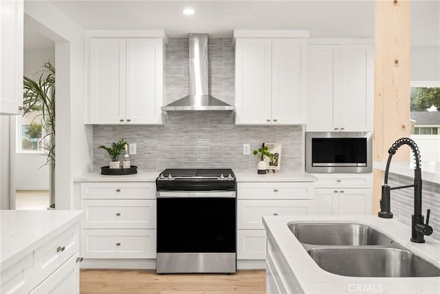 kitchen with a sink, wall chimney range hood, white cabinetry, and stainless steel appliances