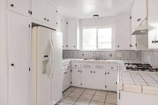 kitchen with under cabinet range hood, a sink, white appliances, white cabinets, and tile counters