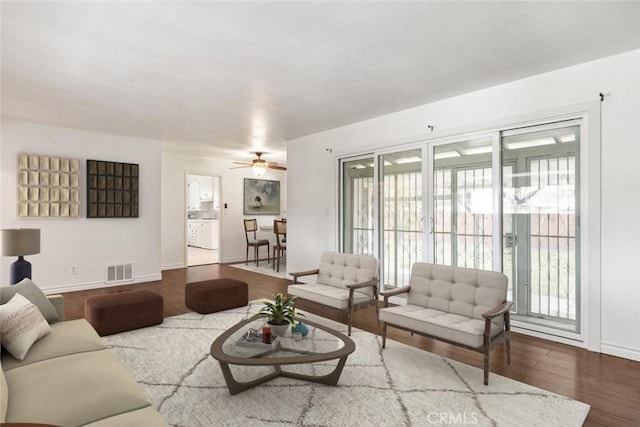 living room with baseboards, wood finished floors, visible vents, and ceiling fan