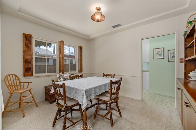 dining area featuring a raised ceiling, light colored carpet, visible vents, and baseboards