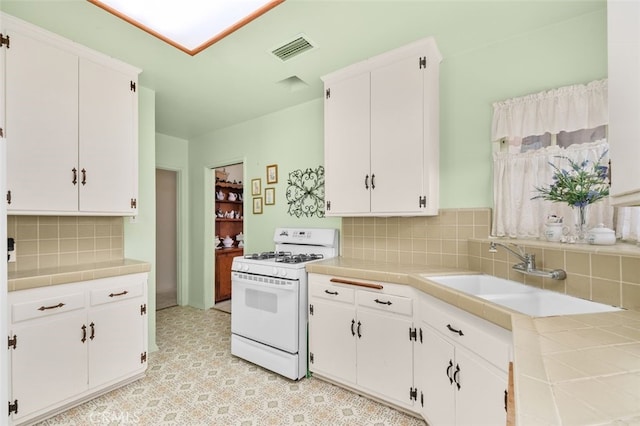 kitchen featuring white gas range, visible vents, tile counters, and a sink