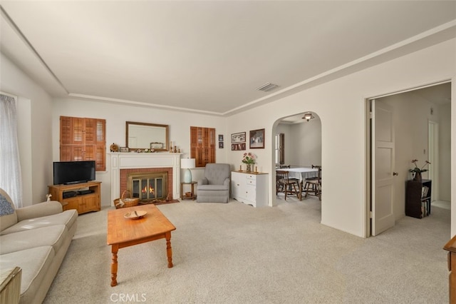 living area featuring visible vents, arched walkways, light carpet, and a fireplace