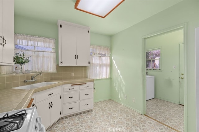 kitchen with backsplash, tile counters, gas range, white cabinetry, and a sink