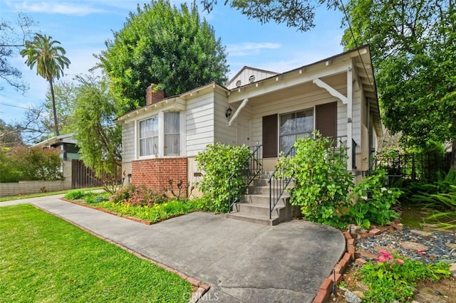 view of front of home featuring brick siding, a chimney, a front yard, and fence