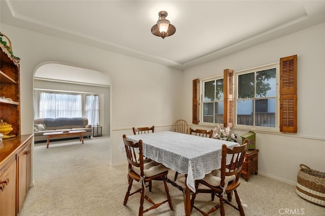 dining room featuring light colored carpet, baseboards, and a tray ceiling