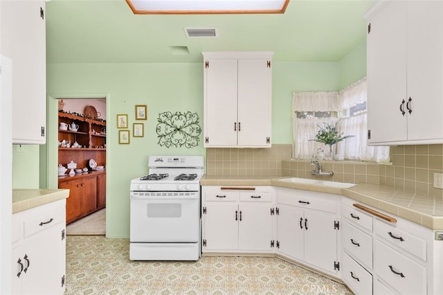 kitchen featuring visible vents, a sink, white cabinets, white range with gas stovetop, and tile counters