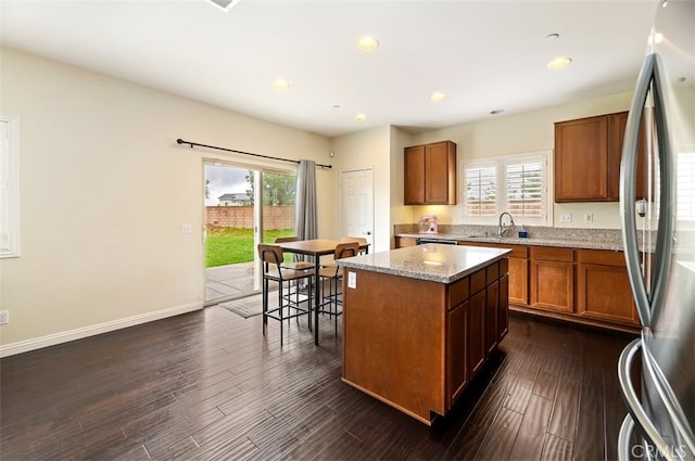 kitchen featuring a sink, dark wood-style floors, a center island, freestanding refrigerator, and brown cabinetry