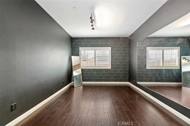 empty room featuring rail lighting, wood finished floors, and baseboards