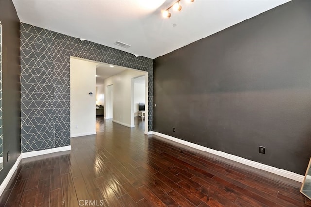 spare room featuring visible vents, baseboards, wood finished floors, and an accent wall