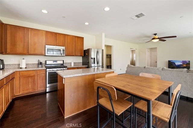 kitchen featuring visible vents, dark wood-type flooring, a ceiling fan, a kitchen island, and appliances with stainless steel finishes