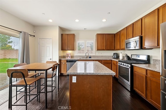 kitchen featuring a center island, dark wood-type flooring, brown cabinets, appliances with stainless steel finishes, and a sink