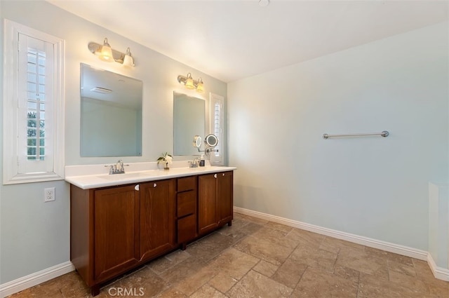 bathroom with a sink, stone finish flooring, baseboards, and double vanity