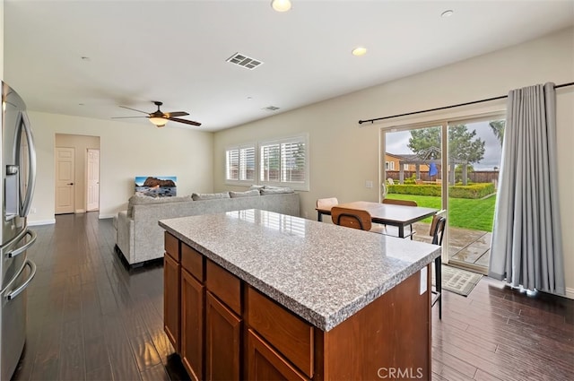 kitchen featuring visible vents, dark wood-type flooring, stainless steel refrigerator with ice dispenser, a kitchen island, and ceiling fan