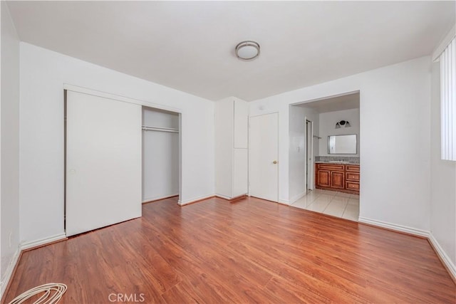 unfurnished bedroom with a closet, baseboards, ensuite bathroom, and light wood finished floors