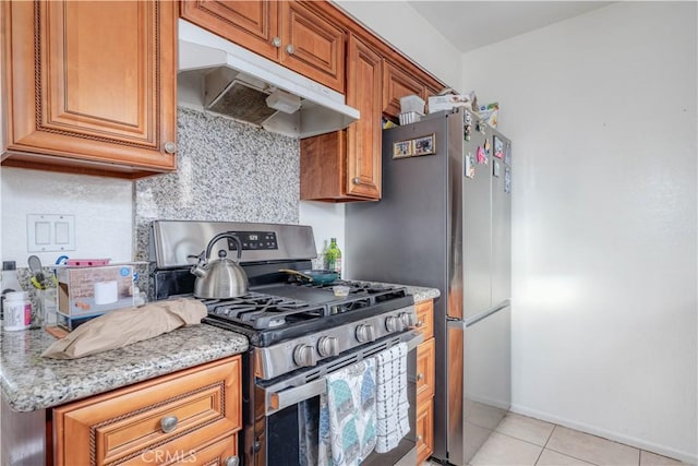 kitchen featuring light tile patterned floors, light stone countertops, stainless steel range with gas cooktop, decorative backsplash, and under cabinet range hood