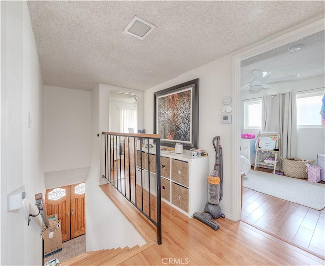 hall featuring an upstairs landing, wood finished floors, and a textured ceiling