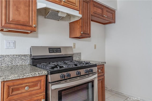 kitchen with under cabinet range hood, stainless steel range with gas stovetop, brown cabinetry, and light stone counters