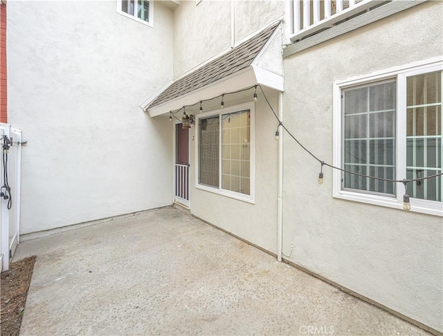 property entrance with a shingled roof, a patio, and stucco siding