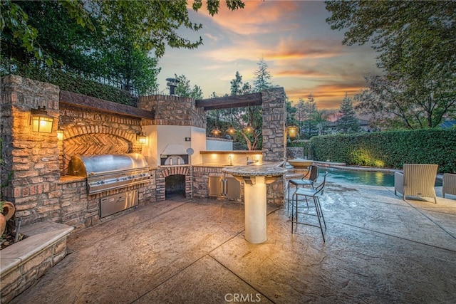 patio terrace at dusk featuring area for grilling and exterior kitchen