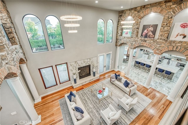 living area with a fireplace, wood finished floors, a high ceiling, and decorative columns