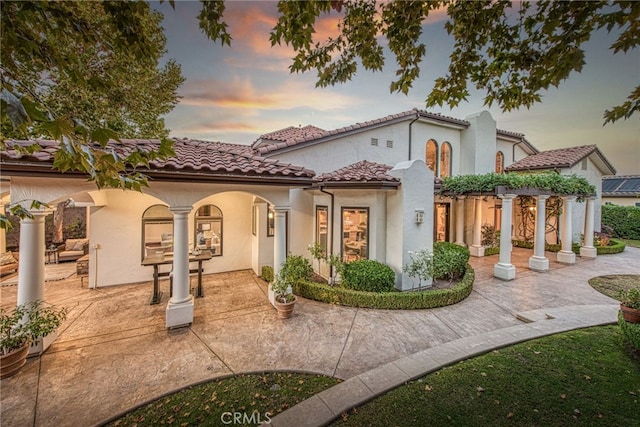 back of house at dusk featuring stucco siding, a patio area, and a tiled roof