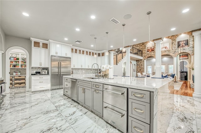 kitchen featuring decorative columns, gray cabinets, a sink, appliances with stainless steel finishes, and a warming drawer