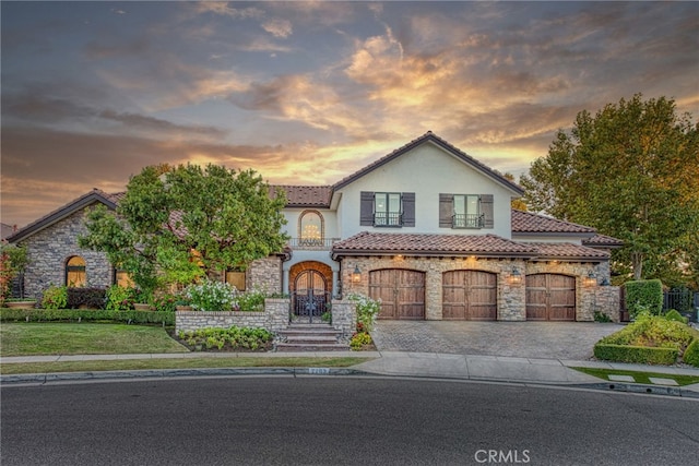 view of front of home with an attached garage, stucco siding, stone siding, a tile roof, and decorative driveway