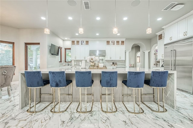 kitchen featuring visible vents, decorative columns, arched walkways, stainless steel built in fridge, and backsplash