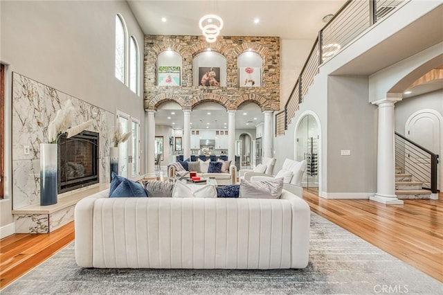 living room featuring a high end fireplace, baseboards, a towering ceiling, wood finished floors, and ornate columns