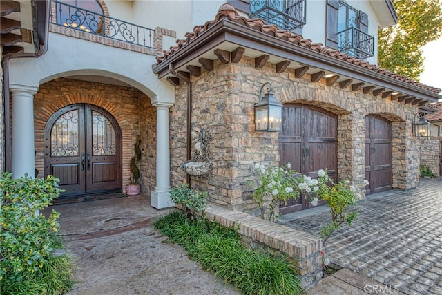 entrance to property with a balcony, french doors, stone siding, and stucco siding