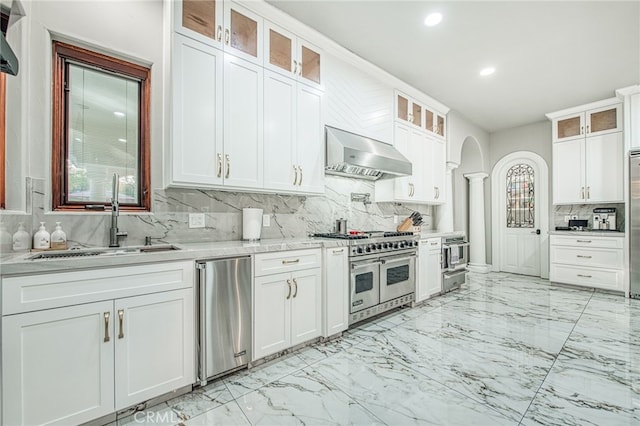 kitchen featuring extractor fan, arched walkways, marble finish floor, stainless steel appliances, and a sink