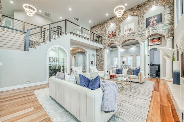 living area featuring visible vents, wood finished floors, ornate columns, and a towering ceiling