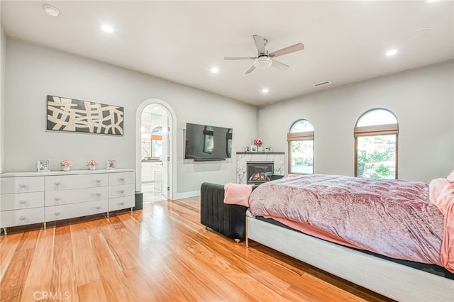 bedroom with light wood-type flooring, ensuite bathroom, a glass covered fireplace, recessed lighting, and arched walkways