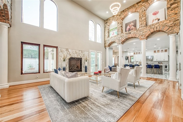 living room with decorative columns, a high end fireplace, and light wood finished floors